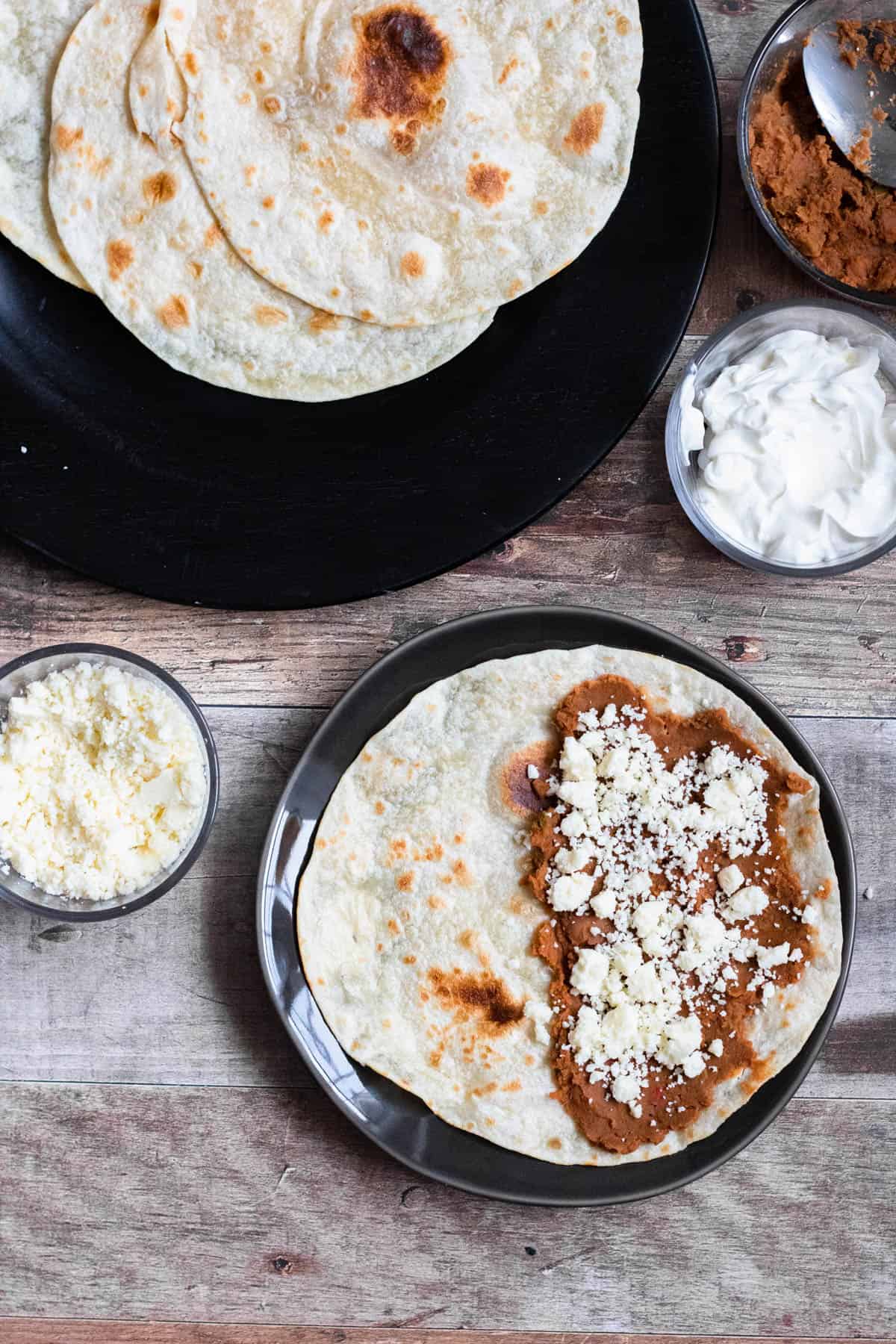 As you continue to prepare a Baleadas Hondurenas, sprinkle cotija cheese over the refried beans on the tortilla. 