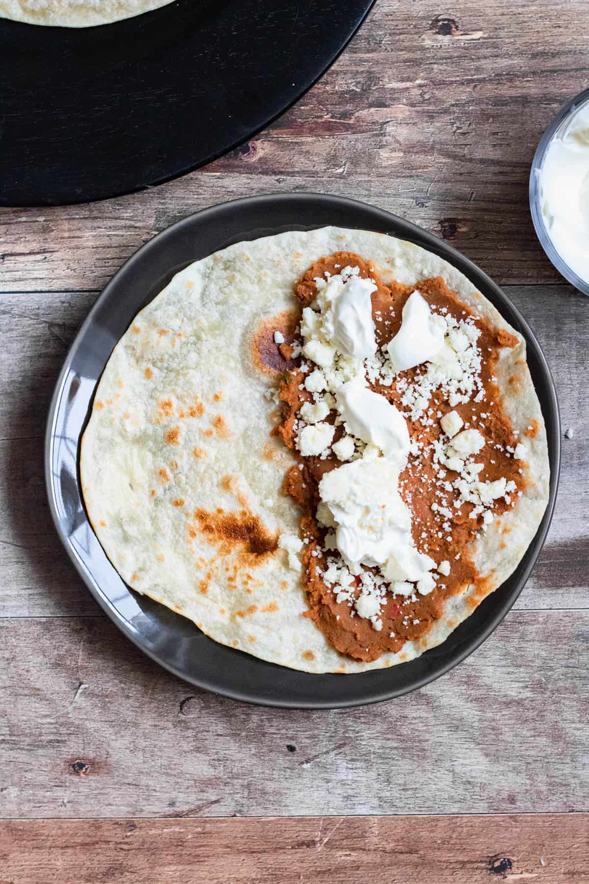Dollops of sour cream are added to Baleadas Hondurenas over the refried beans and cotija cheese. 