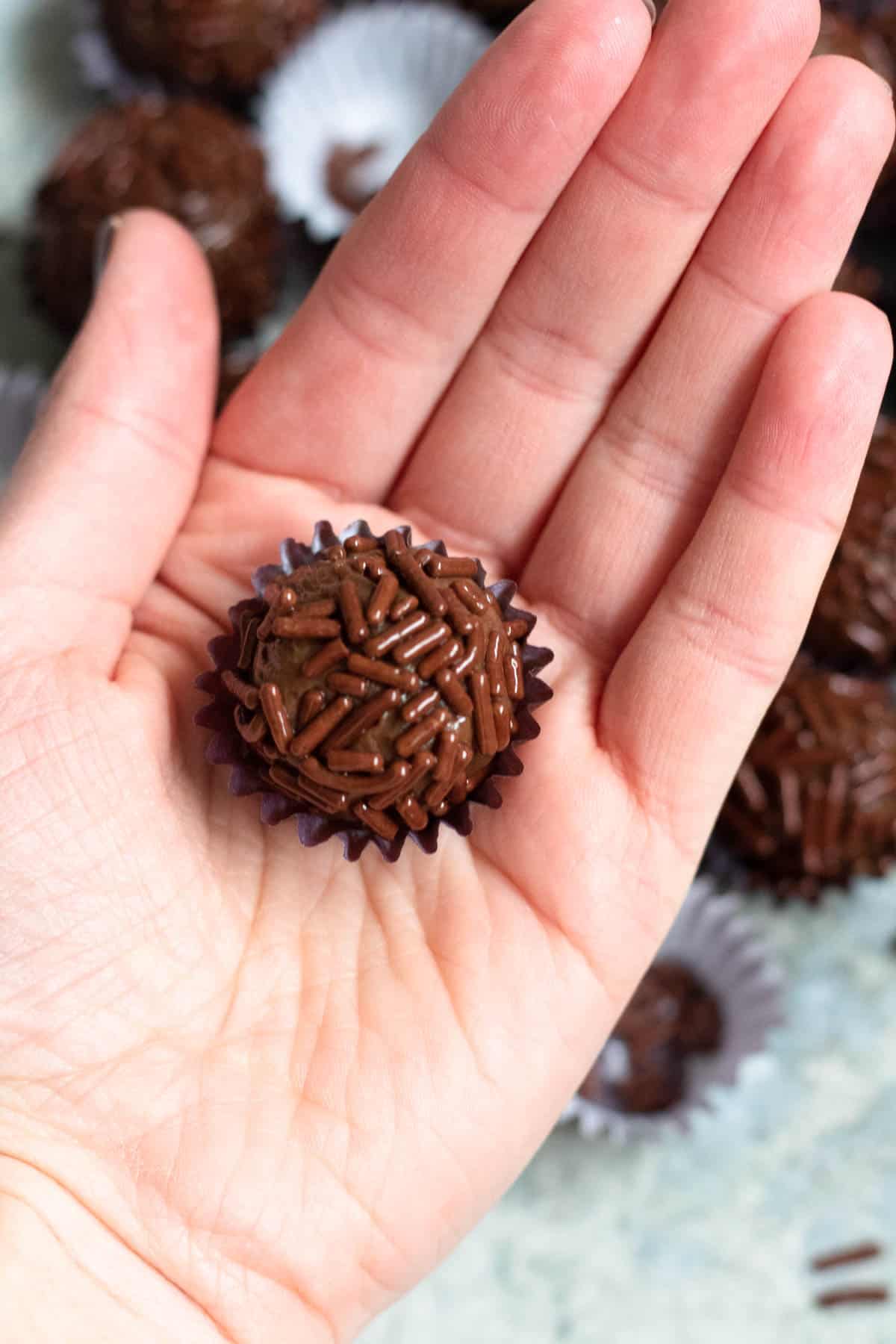 A Brigadeiro in a paper cup, sitting in the palm of a hand. 