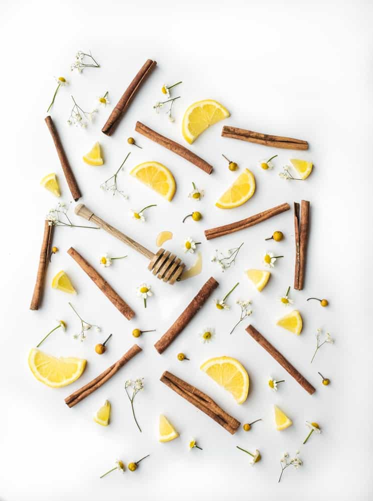 Cinnamon bark, lemon slices and small daisies arranged in a pattern. 