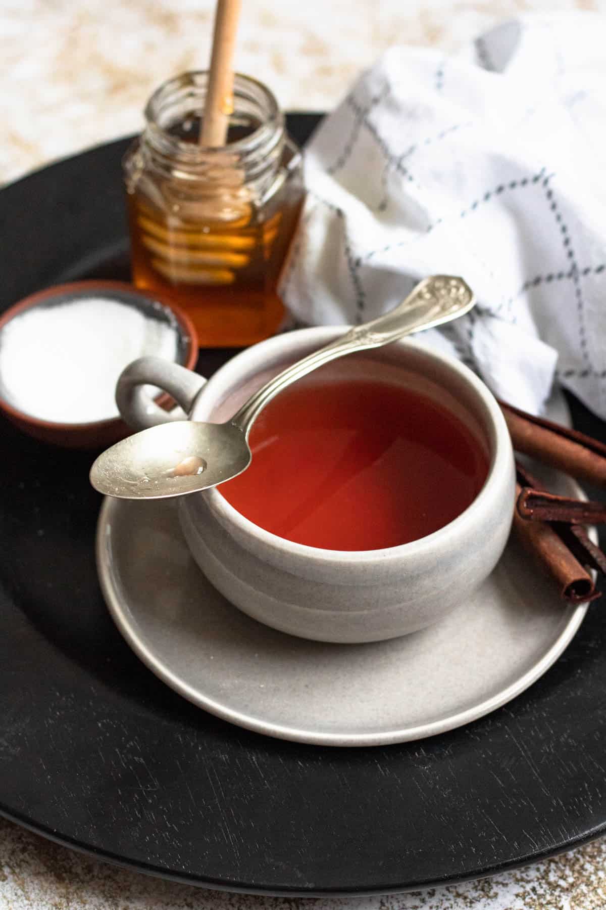 Teaspoon resting over the tea cup sitting on a saucer with cinnamon bark. 