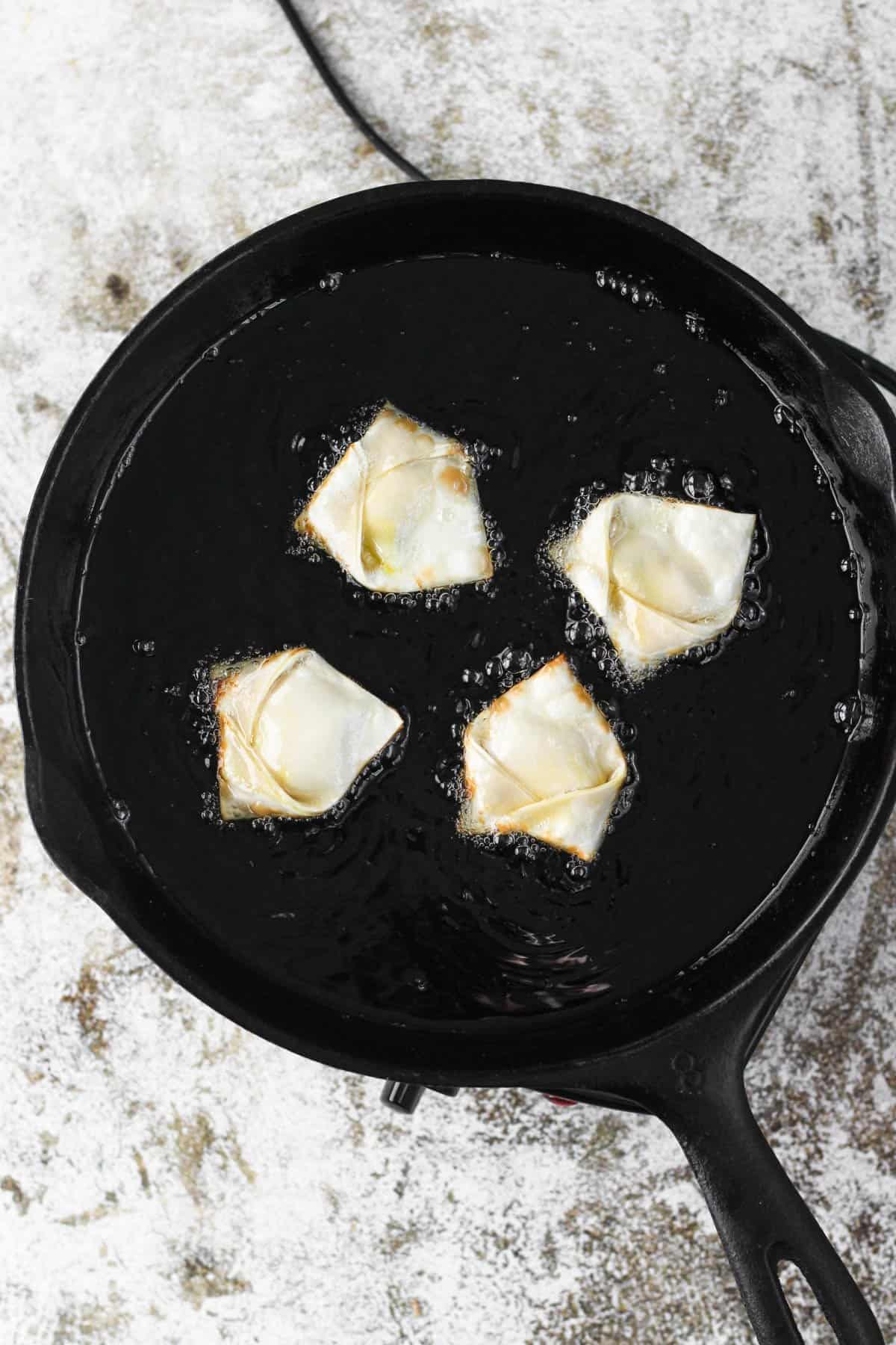 Cast iron skillet with hot vegetable oil and crab rangoons bubbling up on one side to a crispy texture. 