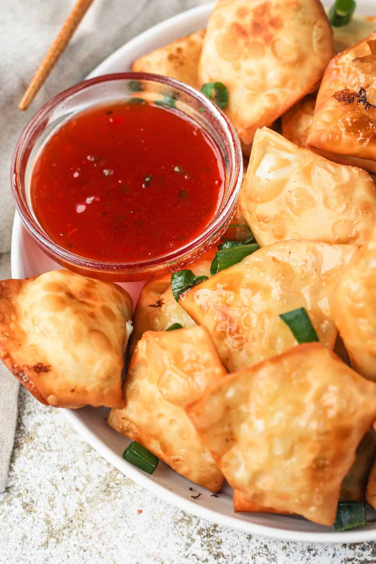 Plate of crab rangoons on a plate with sweet and sour dipping sauce on the side. 