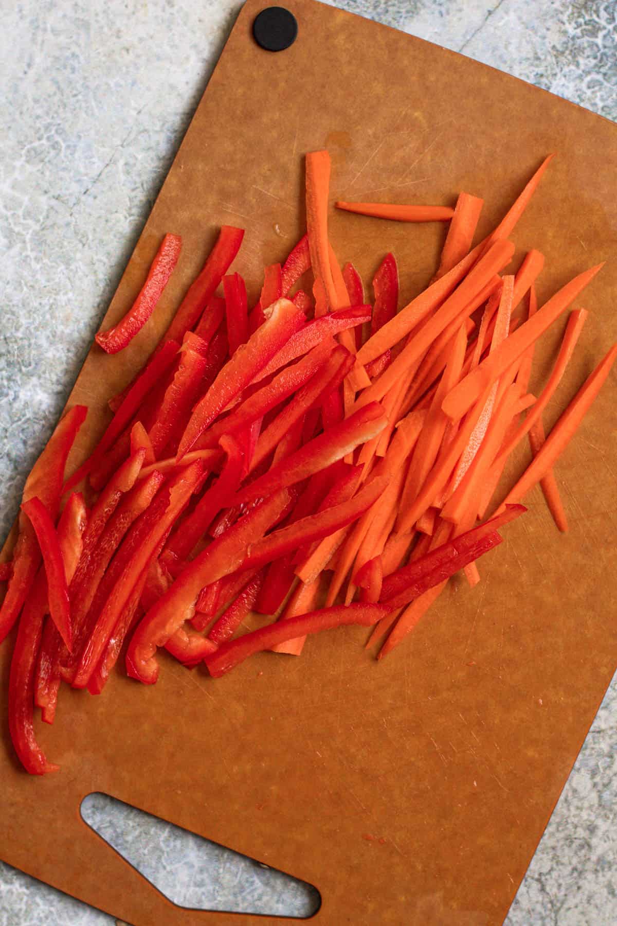 Cutting board with julienned red peppers and carrots. 