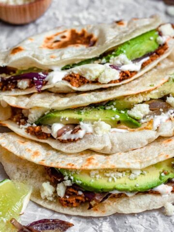3 Baleadas in a pile on parchment paper topped with avocado slices.