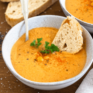 A bowl of chickpea soup with whole cooked chickpeas garnished in the middle and a slice of bread dunking in the bowl.