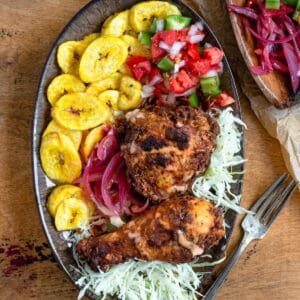 Pollo con Tajadas on a plate, with tostones, then fried chicken, cabbage, sauce, green peppers, and red onions.