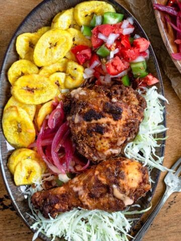 Pollo con Tajadas on a plate, with tostones, then fried chicken, cabbage, sauce, green peppers, and red onions.
