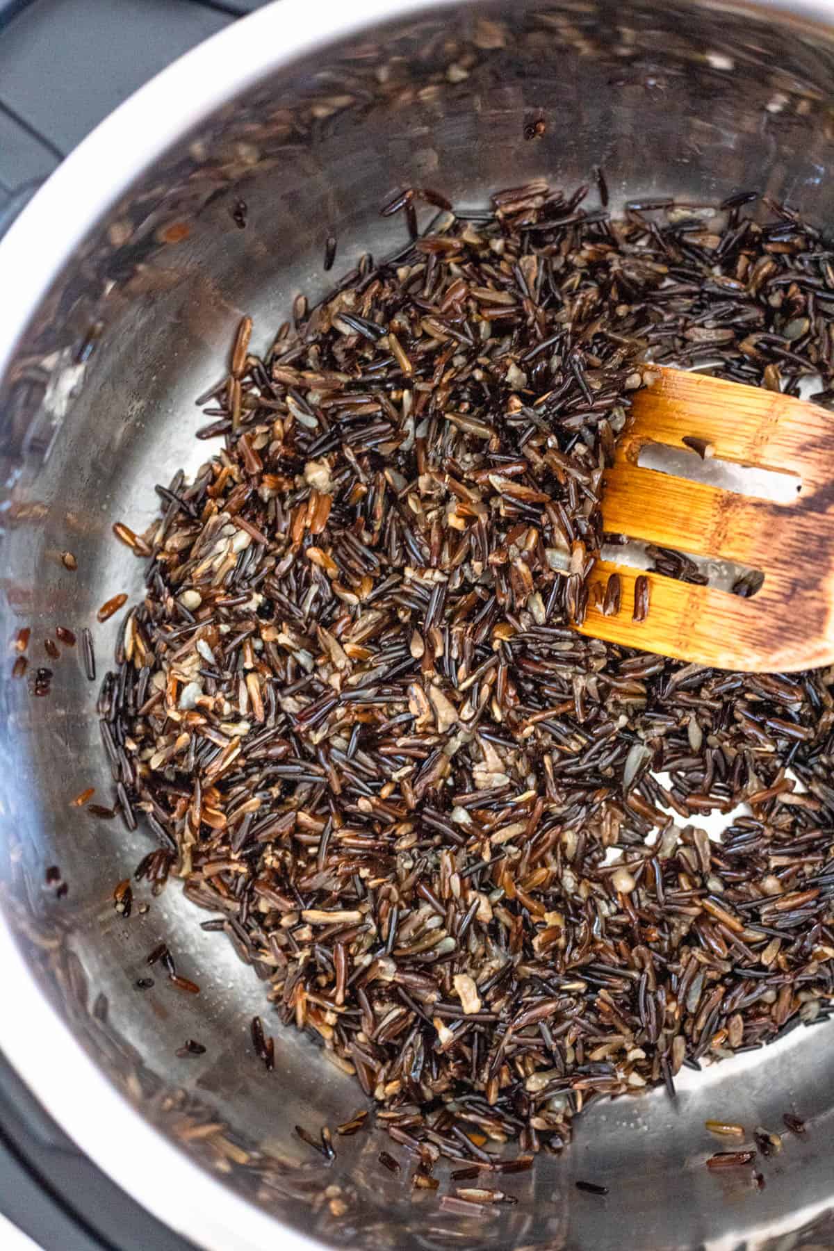 Wooden spoon stirring wild rice in the instant pot. 