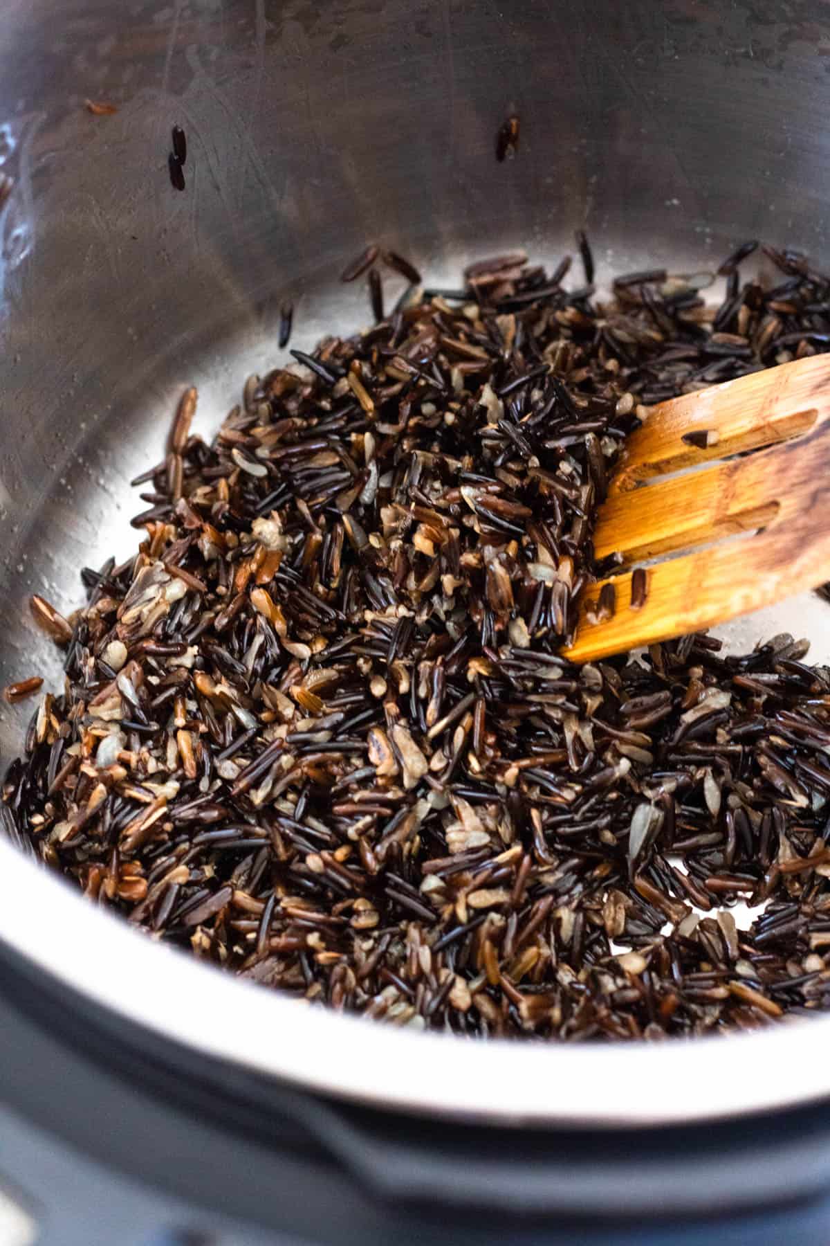 Wood spoon stirring the instant pot wild rice. 