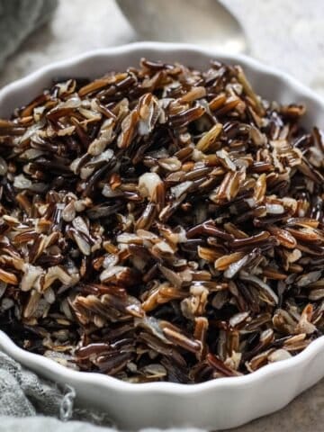 A scalloped bowl holding cooked Wild Rice with a spoon in the background.