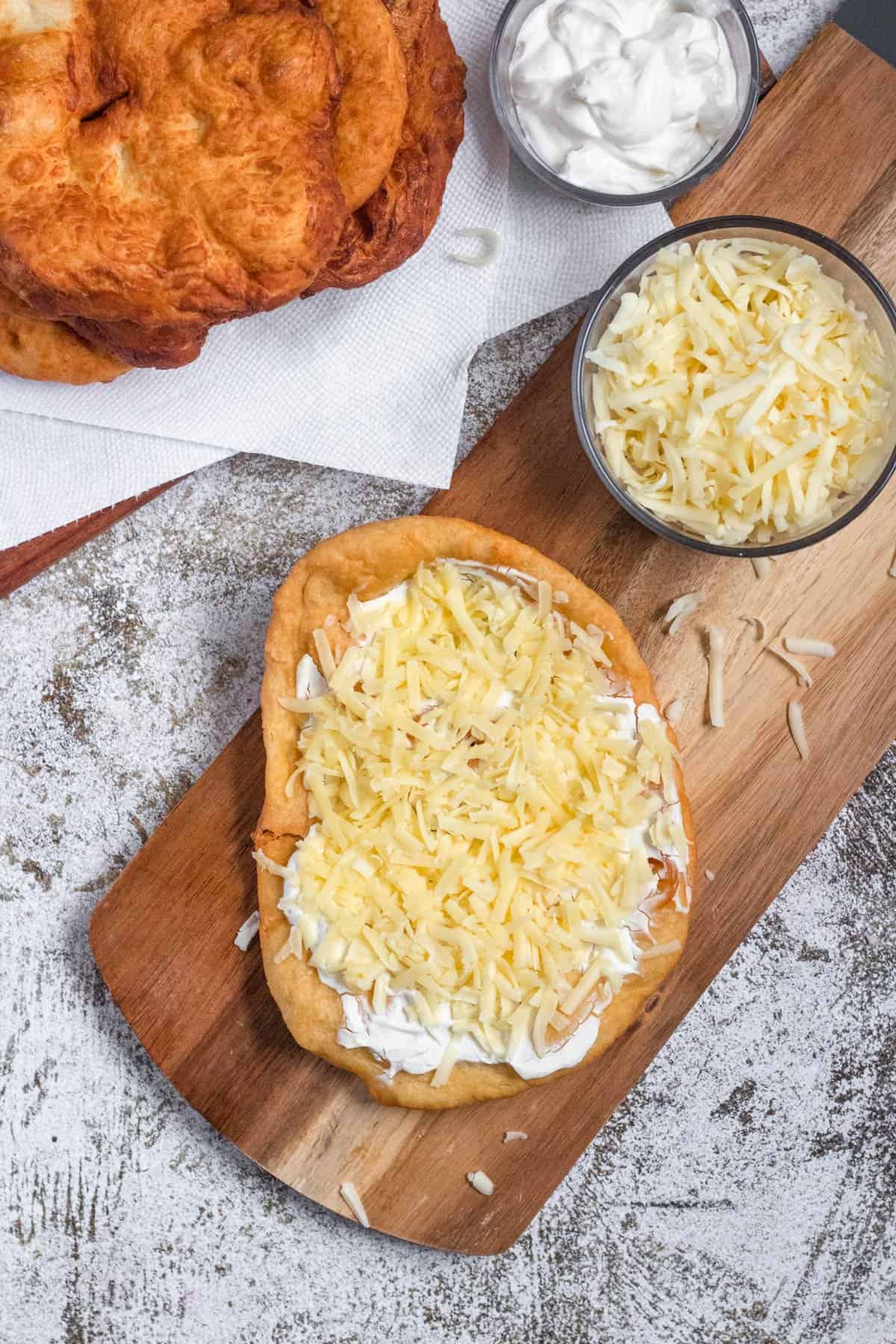 A lango sitting on a cutting board next to a bowl of cheddar cheese topped with sour cream and cheese. 