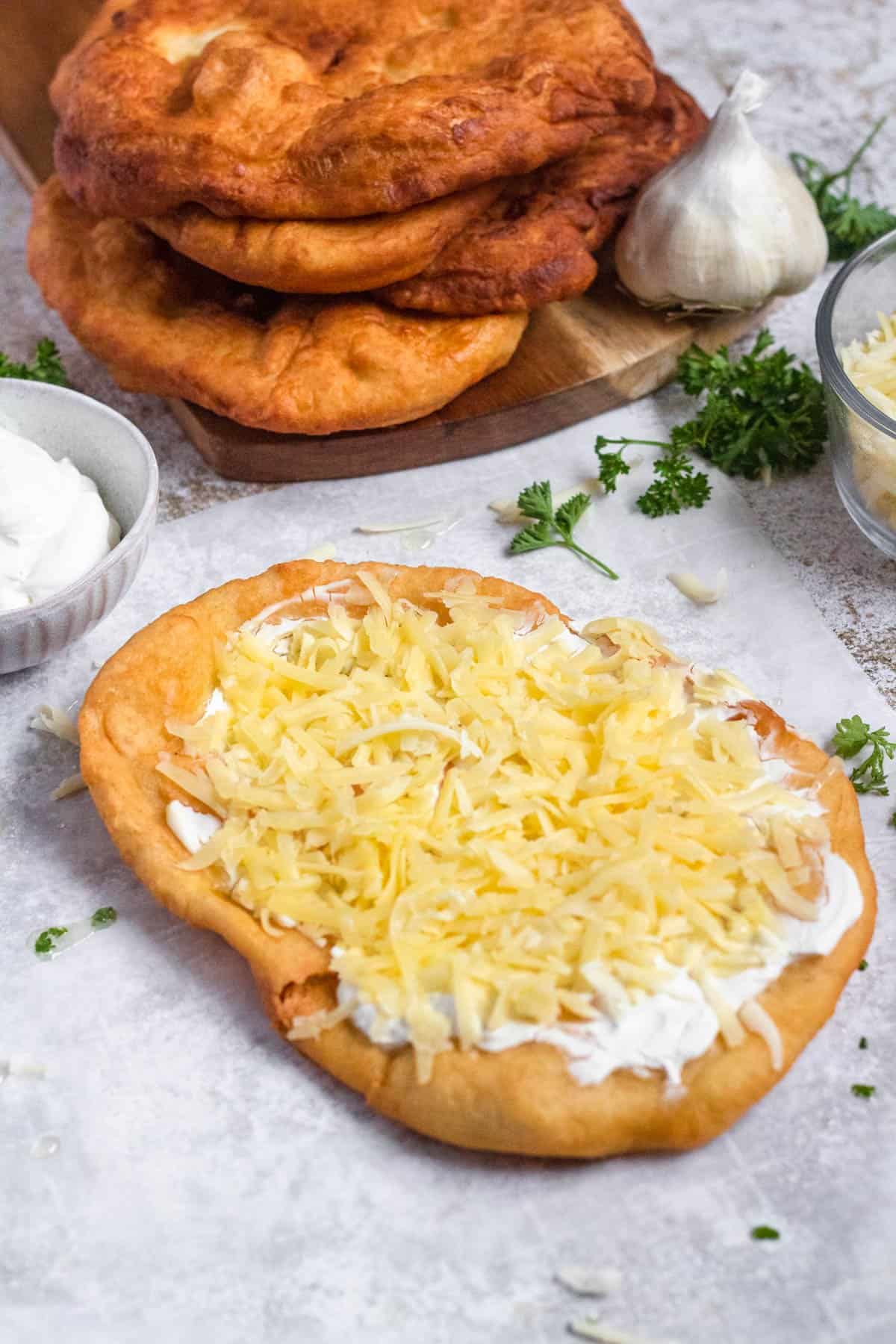 Langos with sour cream and cheese sitting in front of a stack of them ready to serve. 