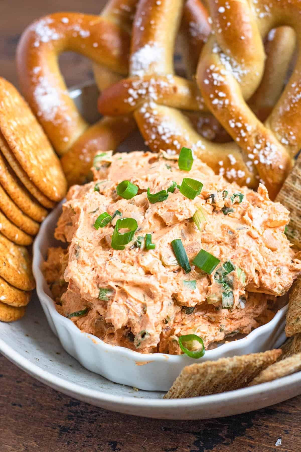 Liptauer dip in a small bowl on a platter with crackers and large soft pretzels. 