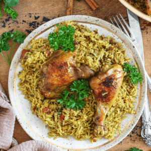 Chicken Machboos served over a bed of seasoned rice and parsley garnished on top.