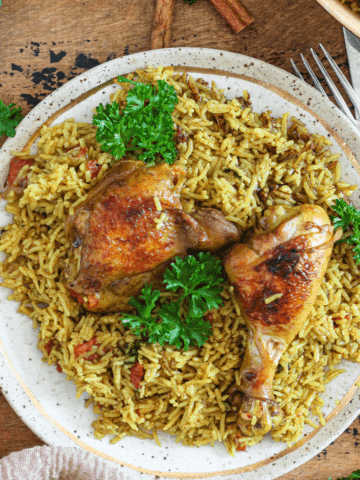 Chicken Machboos served over a bed of seasoned rice and parsley garnished on top.