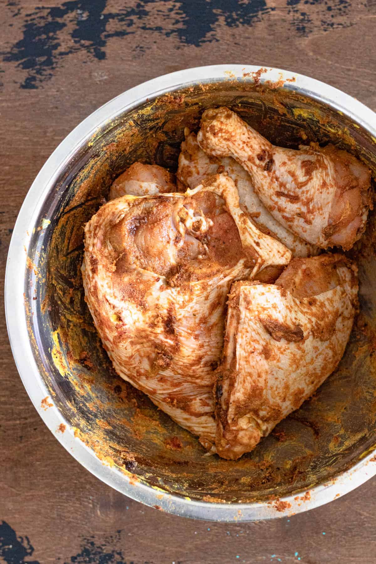 Bowl of raw chicken pieces covered in the spice rub to marinade in preparation for Pollo con Tajadas.  