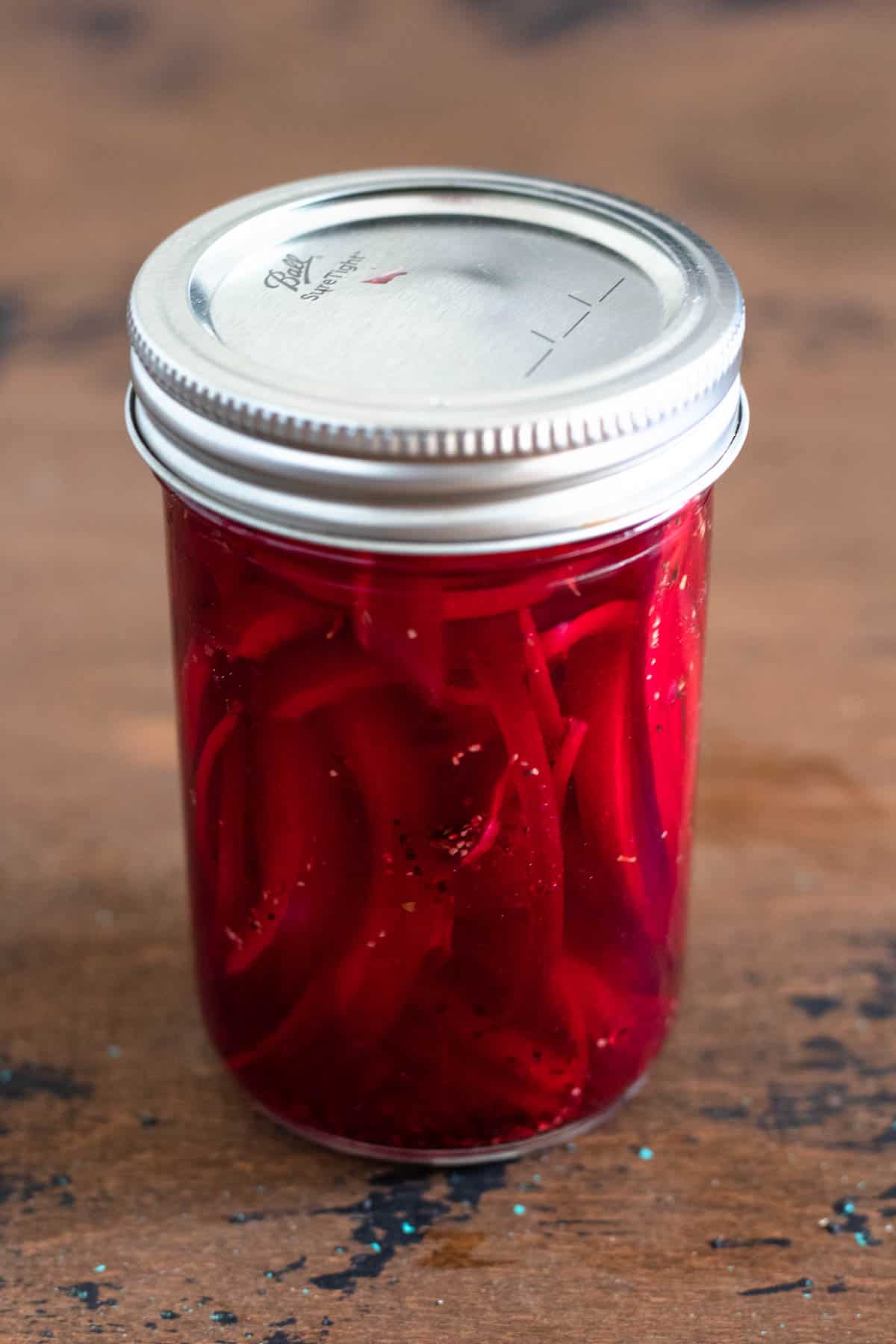Glass jar of onions in pickling ingredients.