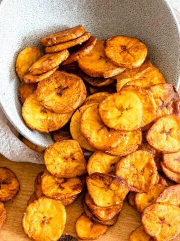 Fried plantain chips spilling out of a serving bowl.