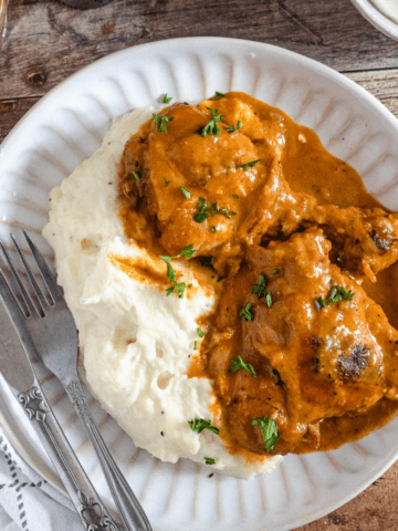Chicken Paprikash in a bowl next to mashed potatoes and serving utensils.