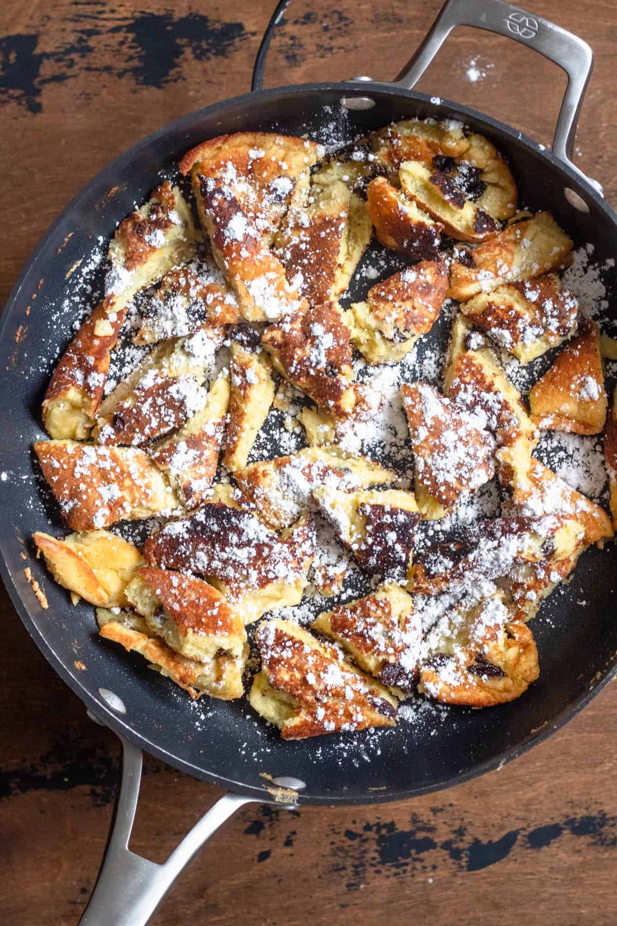 Shredded Kaiserschmarrn in a skillet topped with powdered sugar. 