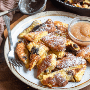 Slices of Kaiserschmarrn with powdered sugar on top and a small bowl of applesauce sitting on the plate.