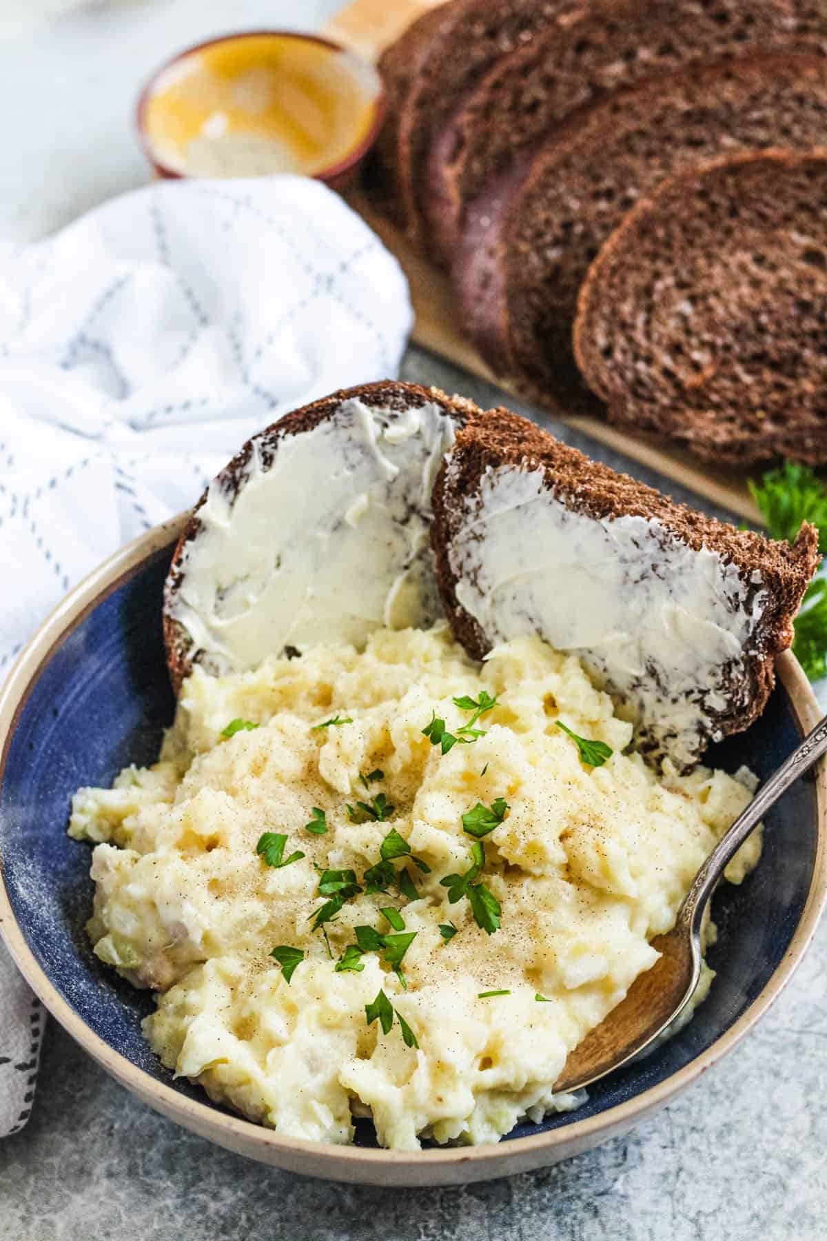A bowl of Plokkfiskur with a spoon and two pieces of buttered rye bread. 