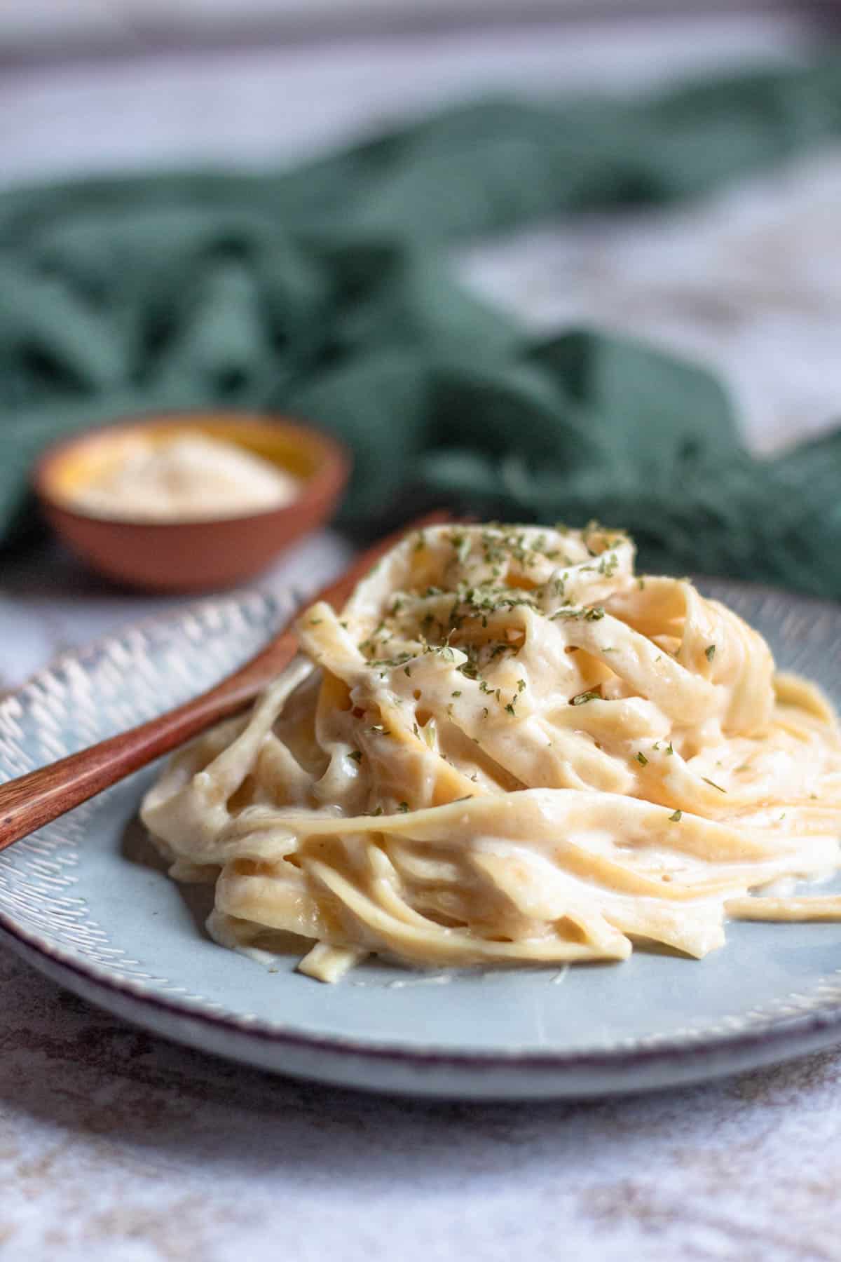 Side view of a serving of instant pot fettucine alfredo served on a plate with chopped parsley garnished over it. 