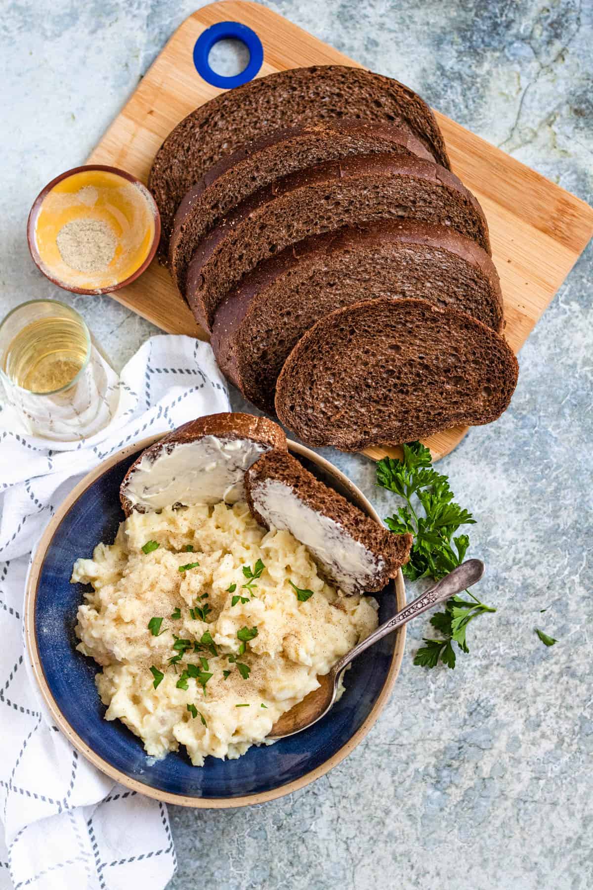 Slices of rye bread on a cutting board and a bowl of Plokkfiskur sitting in front of it with buttered rye bread in the bowl.
