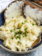 Mashed potatoes and fish mixed together to make Plokkfiskur, topped with pepper and parsley, with rye bread in the background.