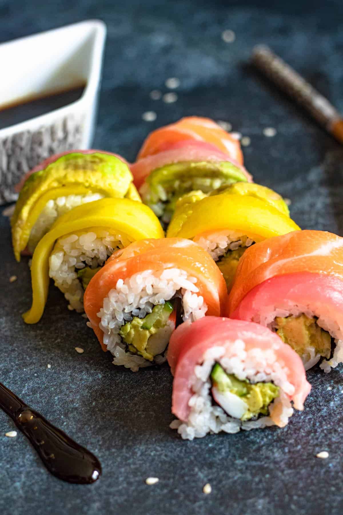 Slices of a Rainbow roll with a side of sauce.