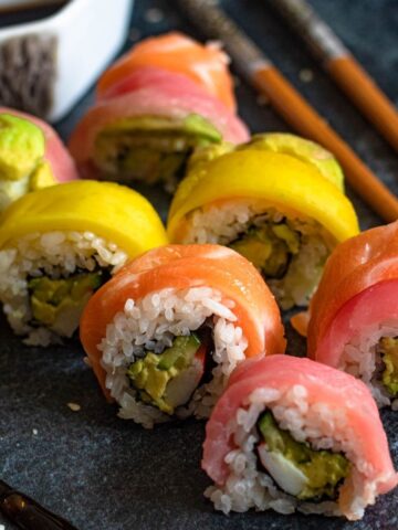 Slices of Rainbow Roll sushi with chopsticks and soy sauce.