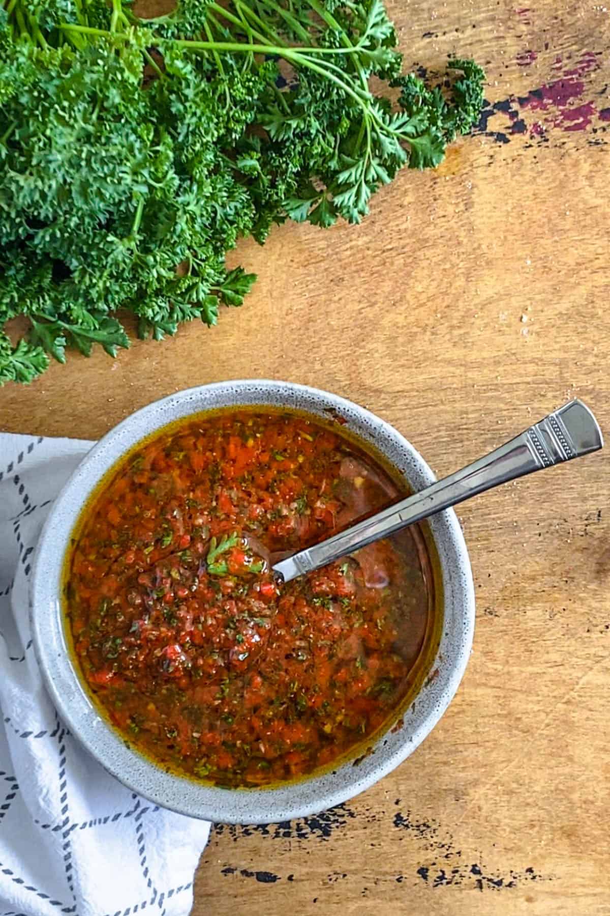 Red chimichurri served in a small bowl with a spoon inside. 