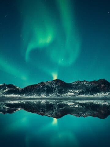 The Northern lights over mountains and water in Iceland.