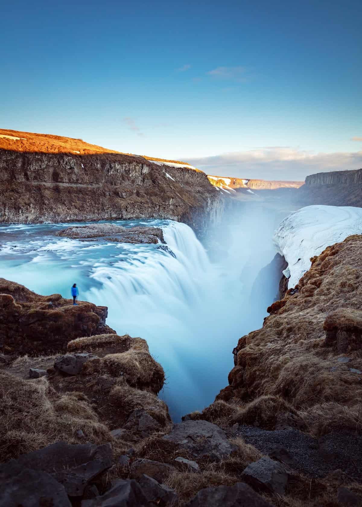 Gullfoss Falls, Iceland with a person standing and watching the water falls as the sun sets.