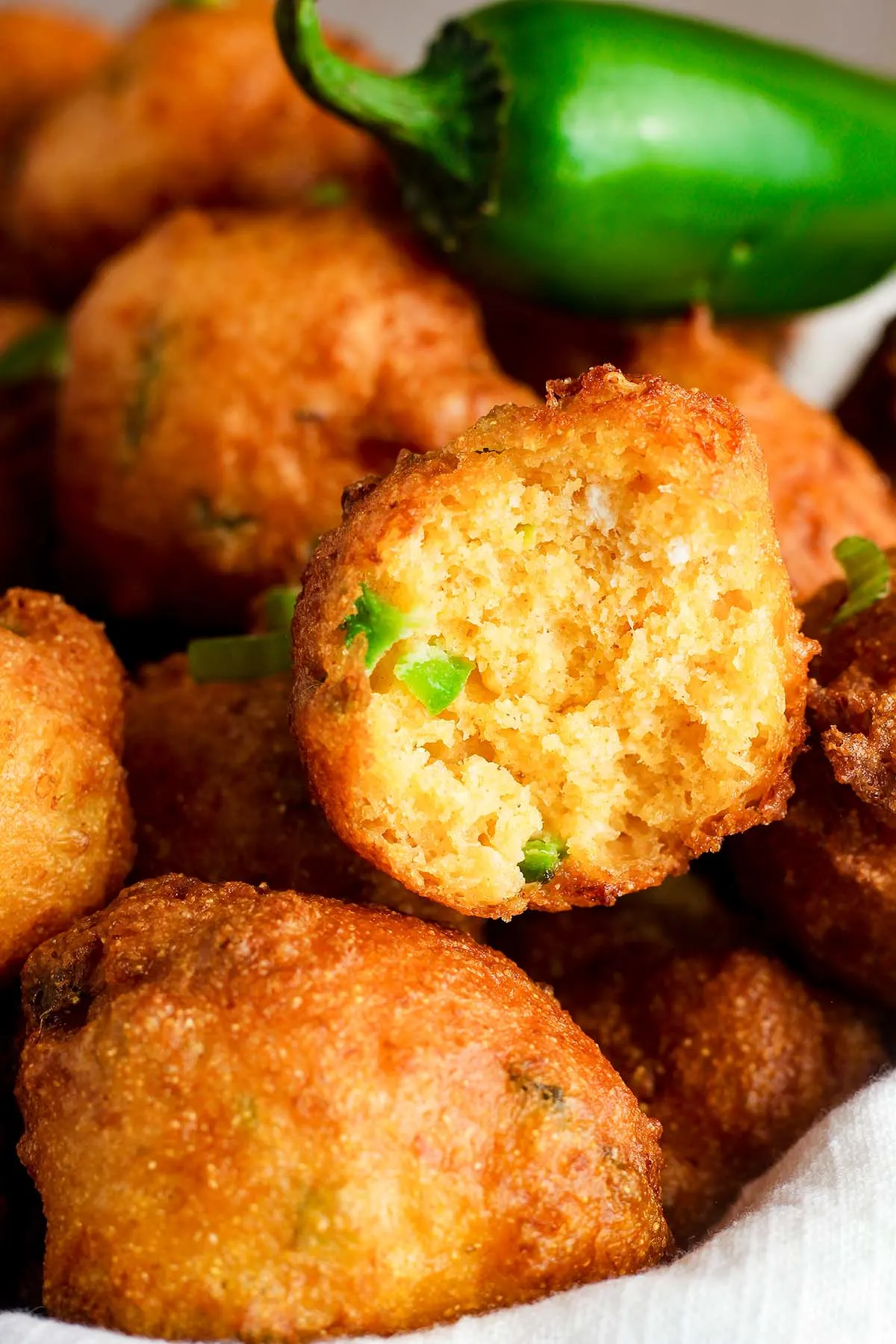 Close up picture of cheddar hush puppies sitting in a towel inside of a basket. 