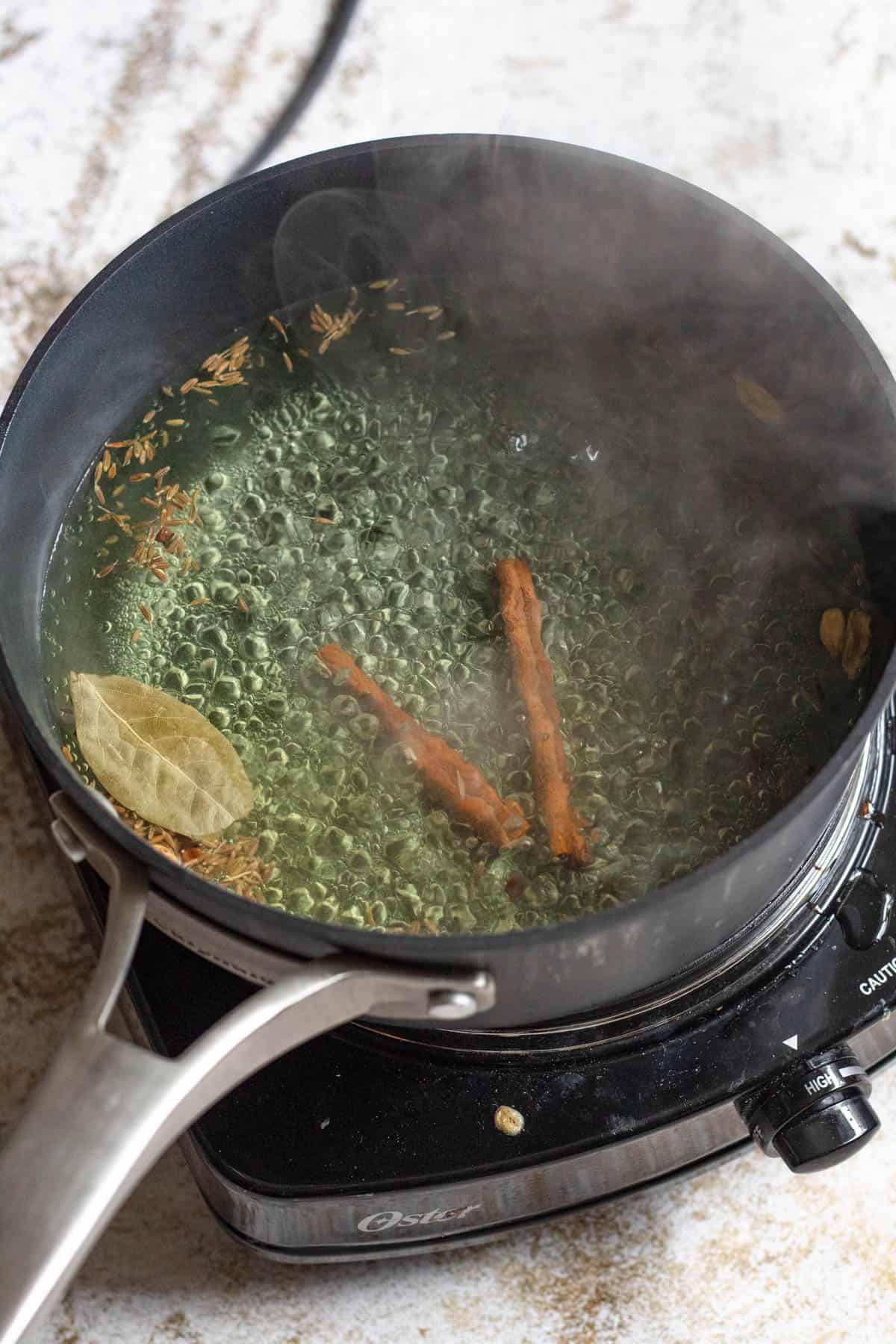 Boiling water with cinnamon sticks and seasonings to start preparing egg biryani. 