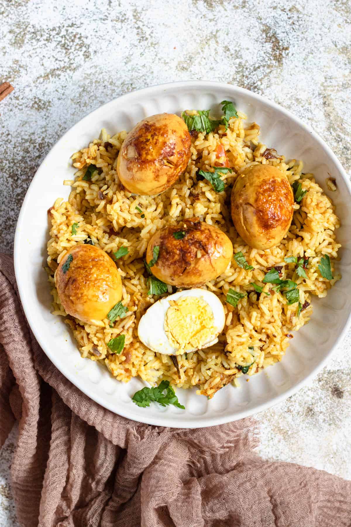 A plate of egg biryani with some whole boiled eggs and some cut in half over the rice. 