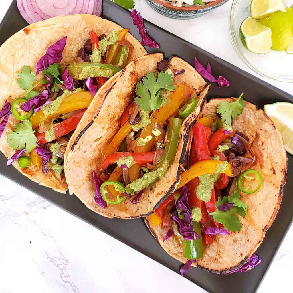 Vegetable fajita tacos served on a rectangular black serving plate. 