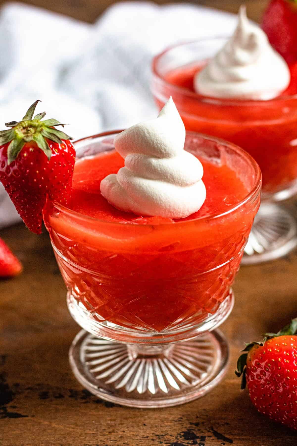 2 glass servings of strawberry kissel garnished with whipped cream and fresh strawberries. 