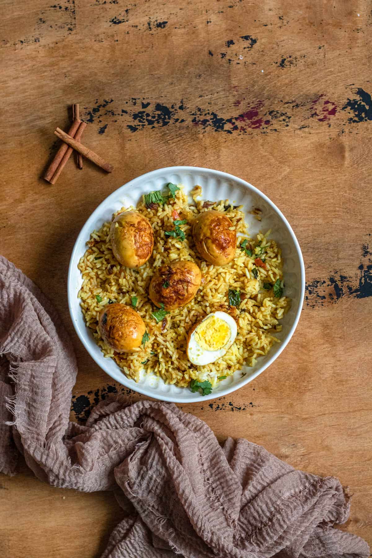 A plate of egg biryani with some cinnamon sticks on the table next to it. 
