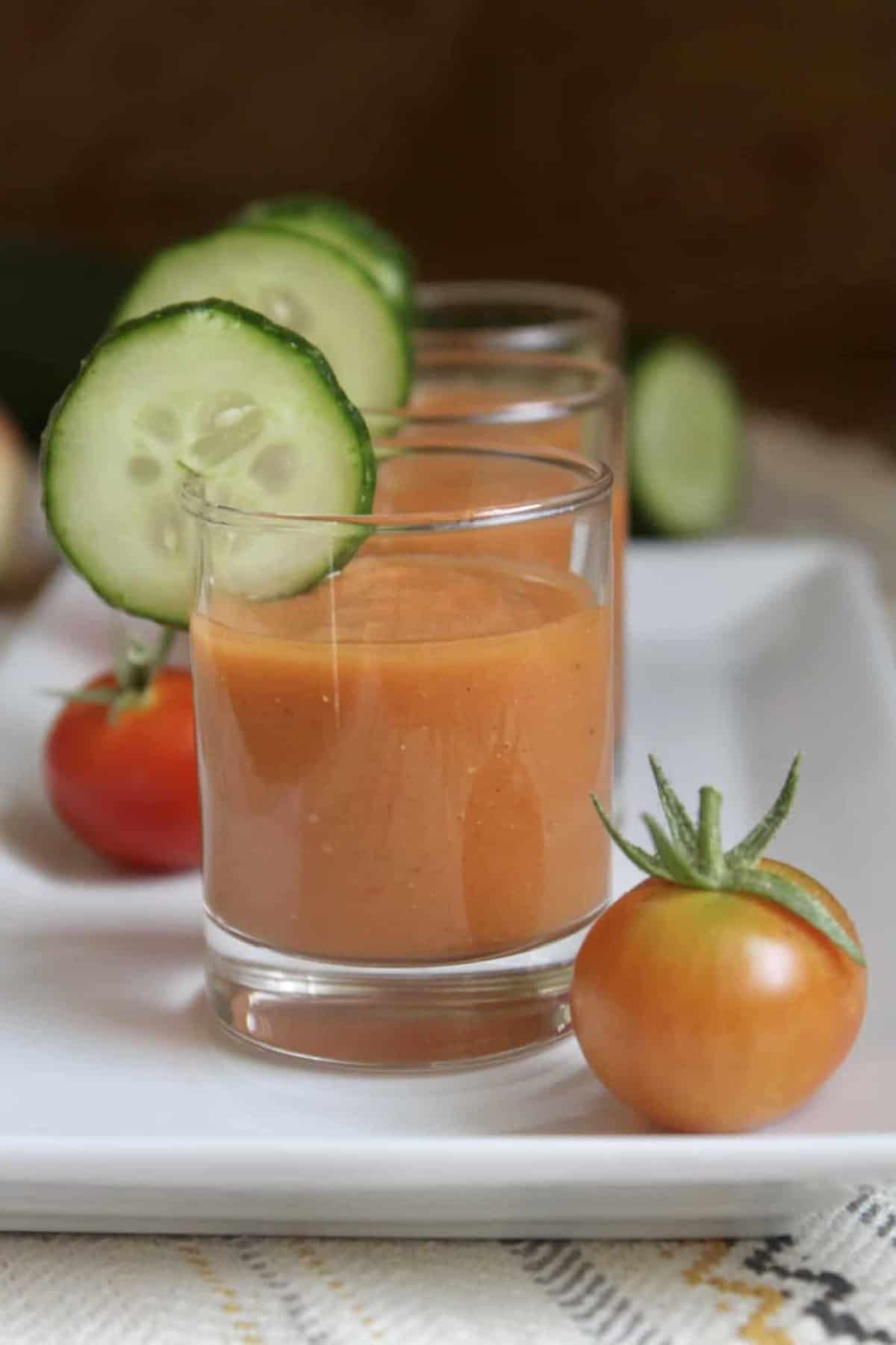 Small glasses of gazpacho served with a garnish of cucumber on each glass. 