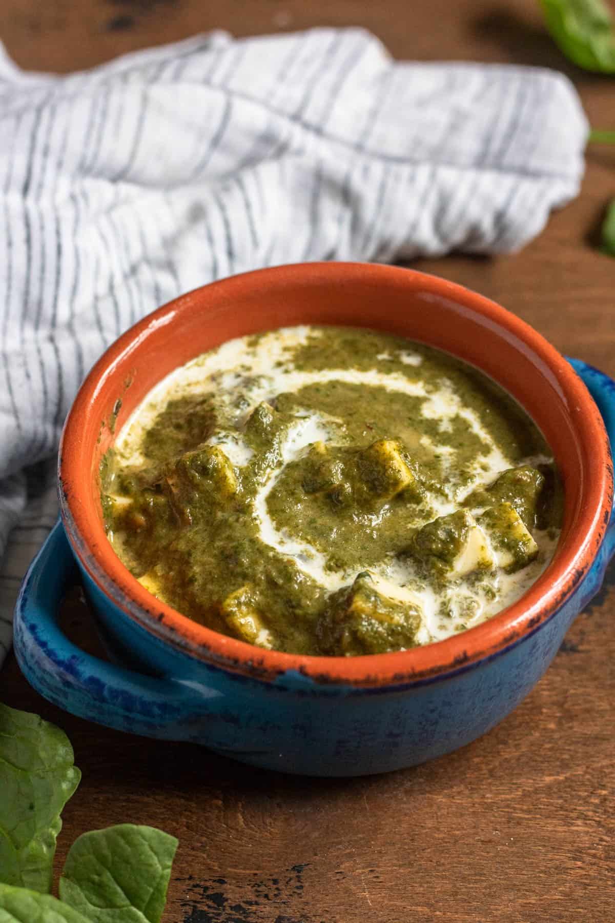 Palak Paneer in an orange and blue bowl with cream on top