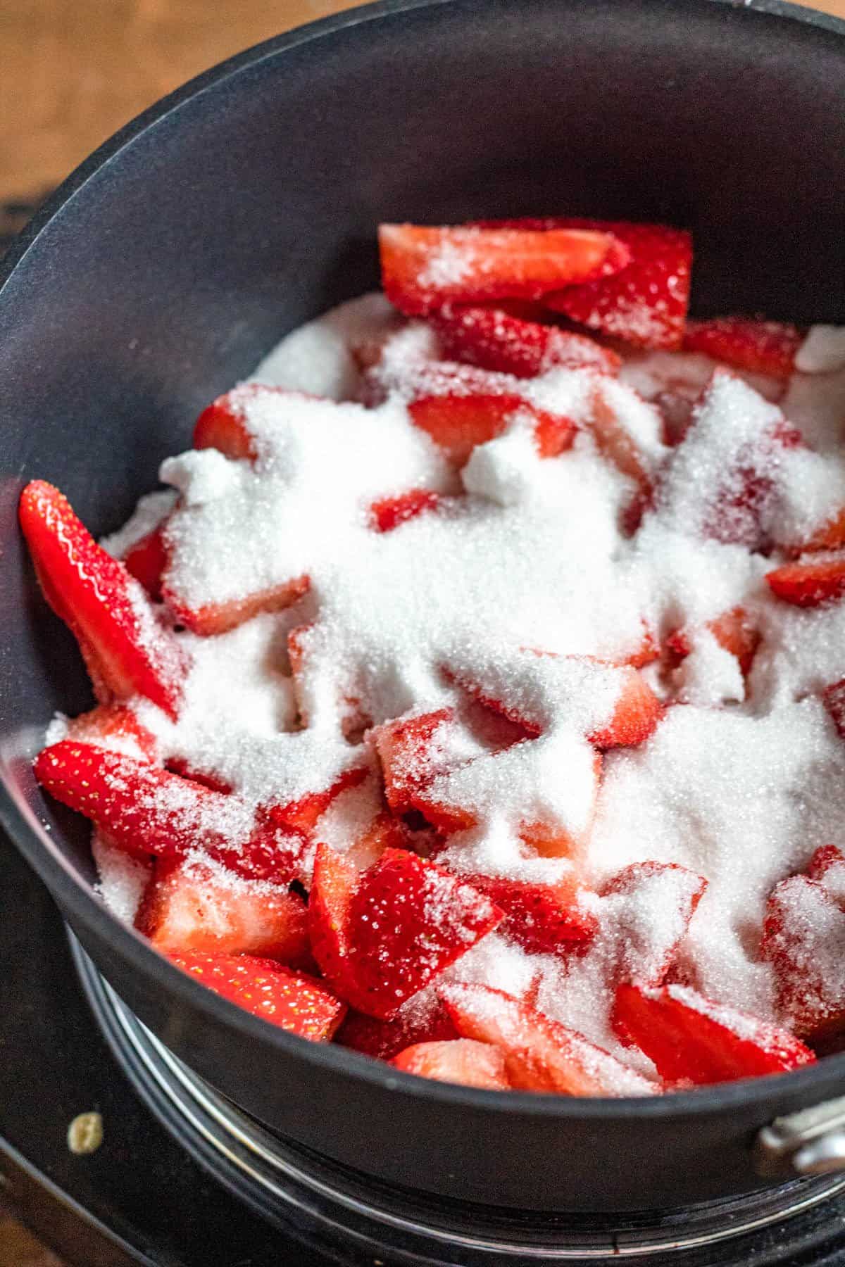 Cut up strawberries in a sauce pan with sugar on top ready to boil. 