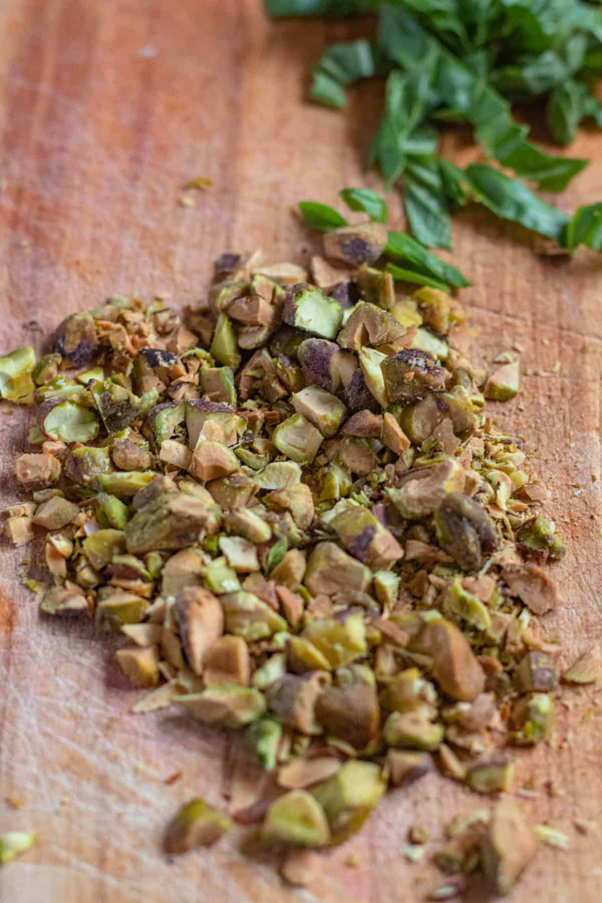 Cutting board with pistachios chopped and fresh basil sliced. 