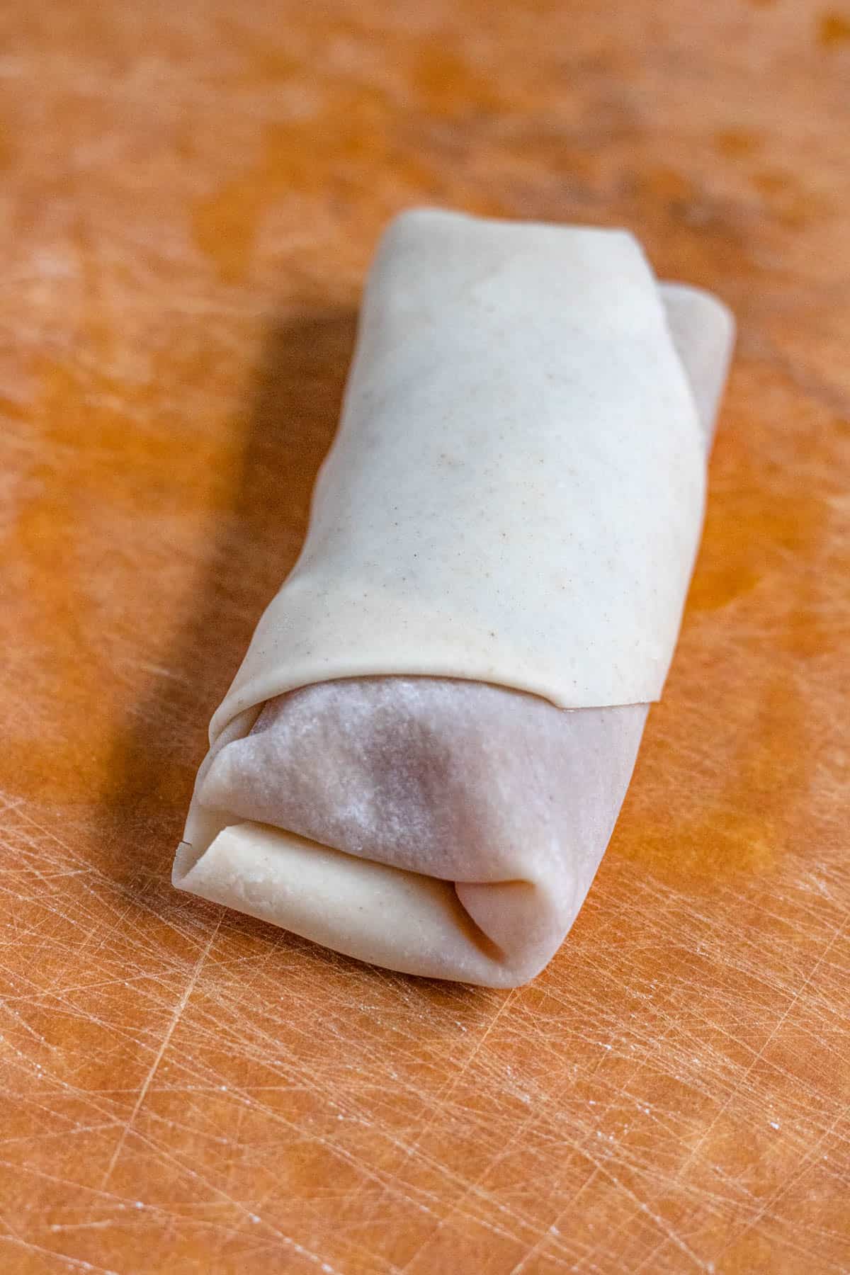 Close up of a rolled egg roll wrapper filled with peach filling to make  peach cobbler egg rolls. 
