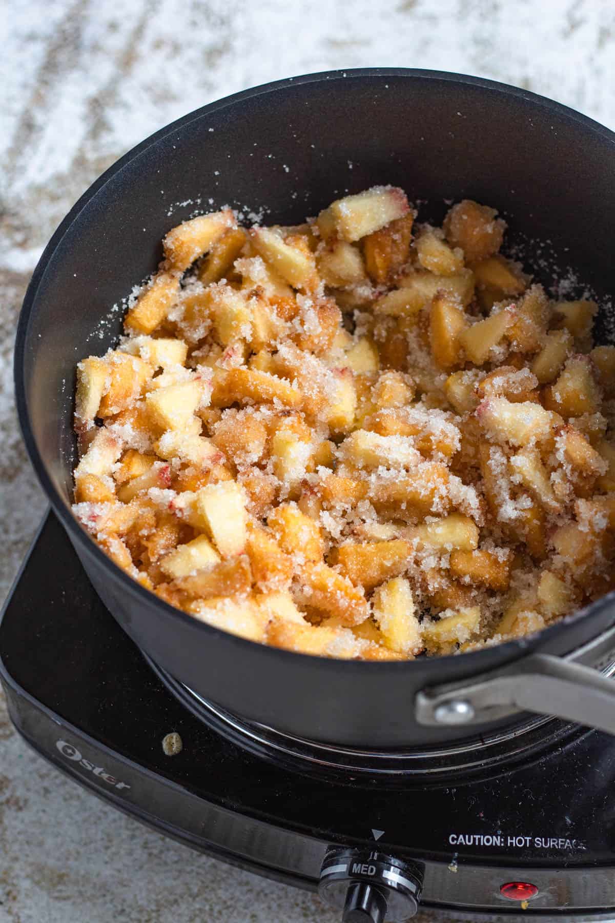 Sauce pan with peaches and sugar combined to make the filling for peach cobbler egg rolls. 