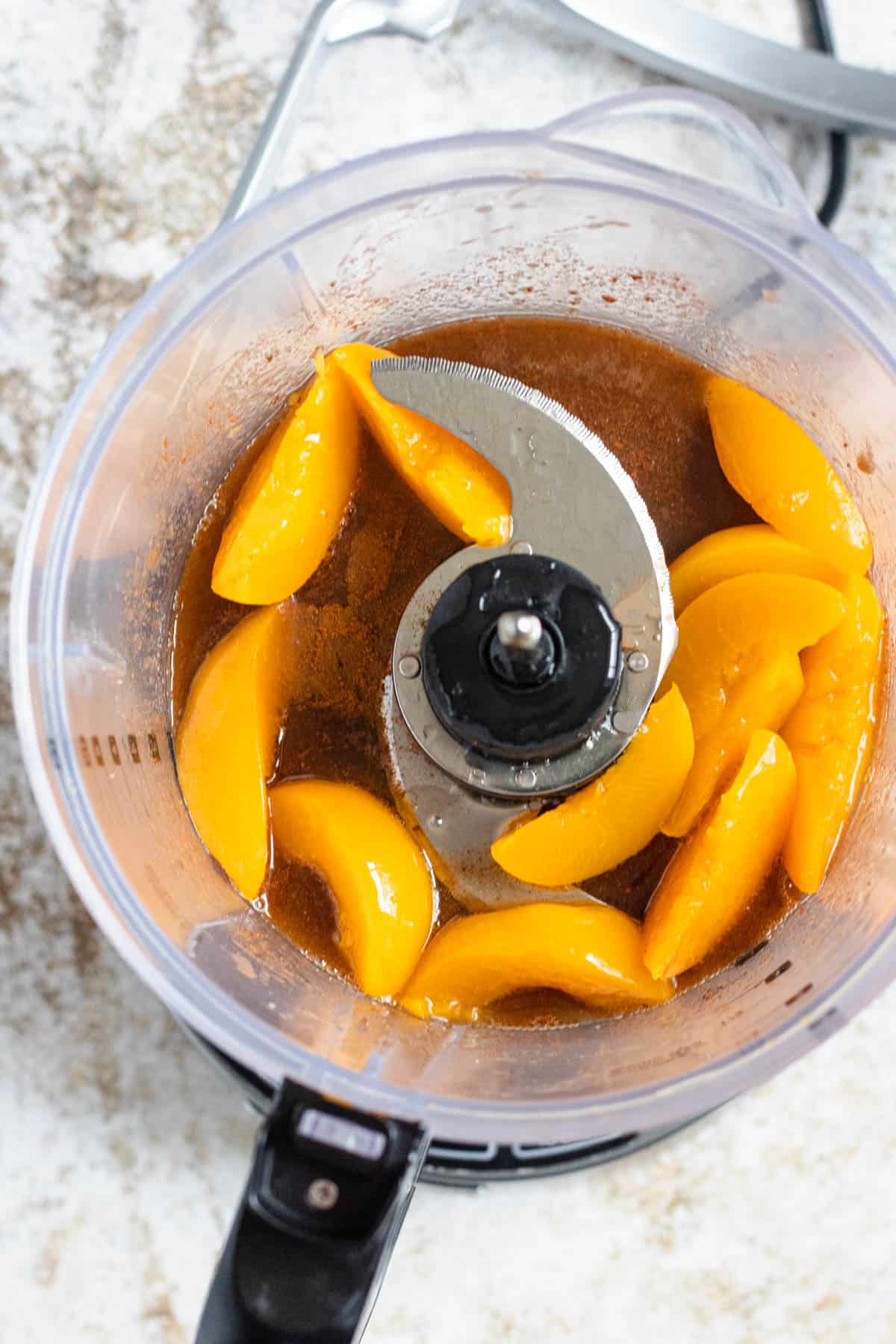 Food processor with seasonings, sugar and canned peaches ready to blend. 