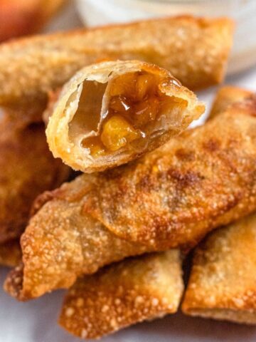 Peach cobbler egg rolls in a pile, with one cut into a cross section.