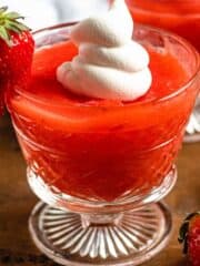 Strawberry kissel in a glass with a whole strawberry on the side with a dollop of cream on top.